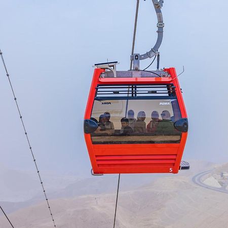 Tolip Resort El Galala Majestic Ain Sukhna Exterior photo The photo shows a red gondola lift suspended in the air, traveling along cables. Inside the gondola, a group of people can be seen. The background features a hazy landscape, possibly mountains or hills, indicating an elevated area. The scene conveys 