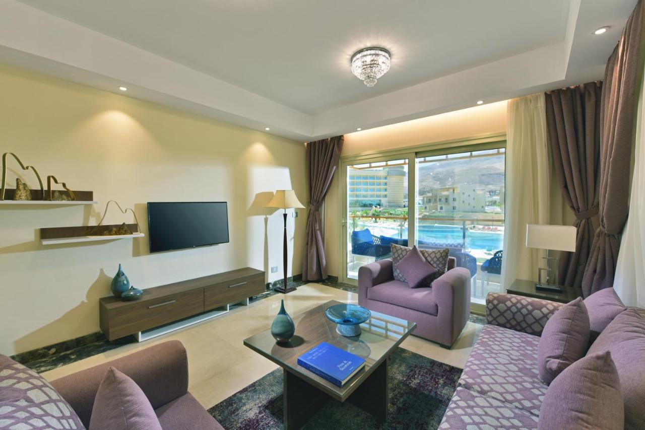 Tolip Resort El Galala Majestic Ain Sukhna Exterior photo The photo shows a modern living room that features a stylish and cozy design. There are two purple sofas with decorative cushions arranged around a coffee table. The coffee table has a blue book and a decorative item on it. A flat-screen TV is mounte