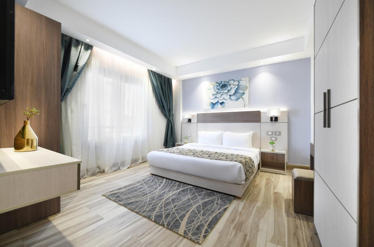 Tolip Resort El Galala Majestic Ain Sukhna Exterior photo The photo shows a modern bedroom with a clean and stylish design. It features a large bed with white bedding positioned against a wall. Above the bed, there is a decorative artwork, possibly a floral design. The room has large windows with sheer curt