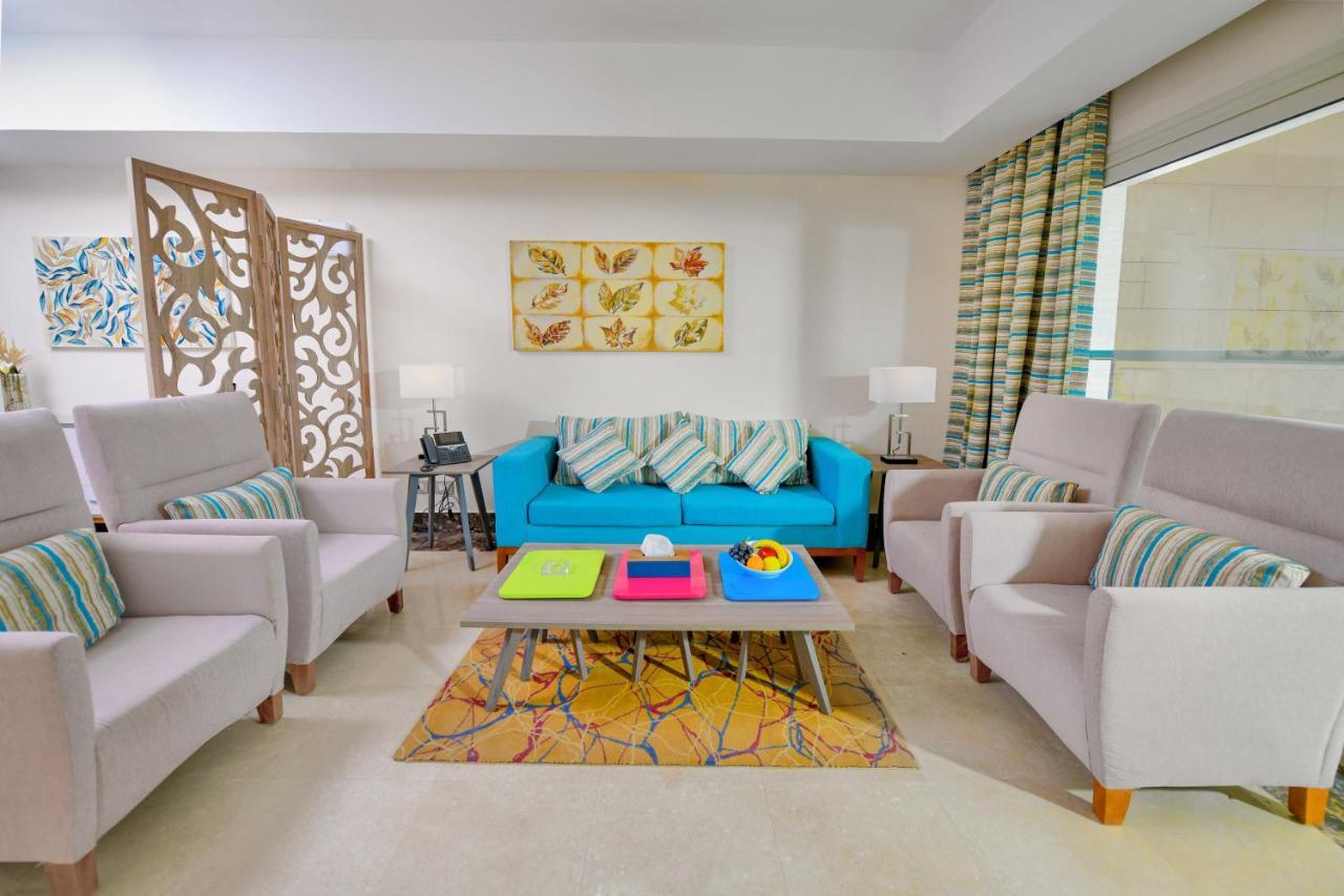 Tolip Resort El Galala Majestic Ain Sukhna Exterior photo The photo shows a stylish and colorful living room. It features a bright blue sofa with patterned cushions, complemented by two light gray armchairs. In front of the sofa, there's a wooden coffee table with vibrant trays in pink, green, and yellow. A