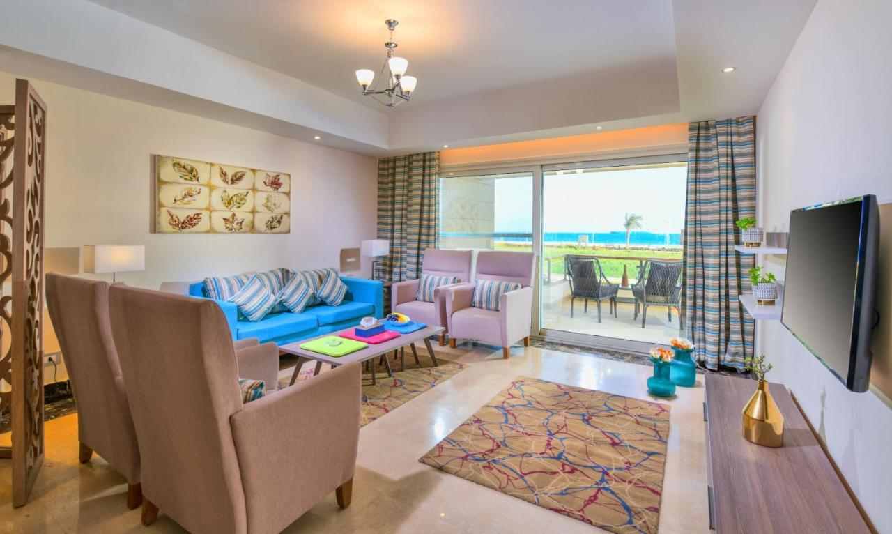 Tolip Resort El Galala Majestic Ain Sukhna Exterior photo The photo shows a bright and modern living room. It features a blue sofa with decorative cushions, two light-colored armchairs, and a coffee table. A large area rug adds warmth to the space, which is decorated with a subtle pattern. The walls have so