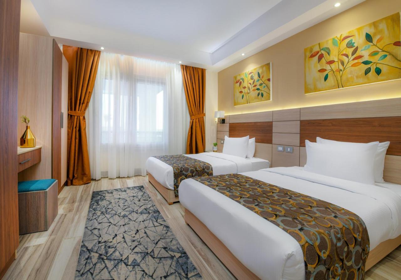 Tolip Resort El Galala Majestic Ain Sukhna Exterior photo The photo shows a modern hotel room with two single beds, each covered with white linens and decorative brown bed throws. The walls are painted in warm colors, and there are two pieces of artwork featuring floral and leaf designs above the beds. The 