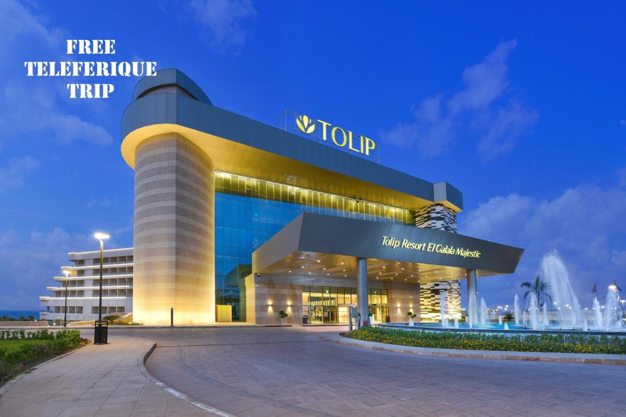 Tolip Resort El Galala Majestic Ain Sukhna Exterior photo The photo shows a modern hotel building named "Tolip Resort & Spa," featuring a sleek architectural design with large glass windows. The hotel is illuminated against a twilight sky, showcasing its prominent signage. In the foreground, there is a well