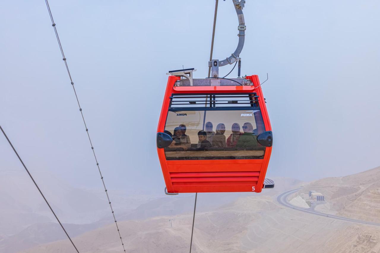 Tolip Resort El Galala Majestic Ain Sukhna Exterior photo The photo shows a red gondola lift suspended in the air, traveling along cables. Inside the gondola, a group of people can be seen. The background features a hazy landscape, possibly mountains or hills, indicating an elevated area. The scene conveys 