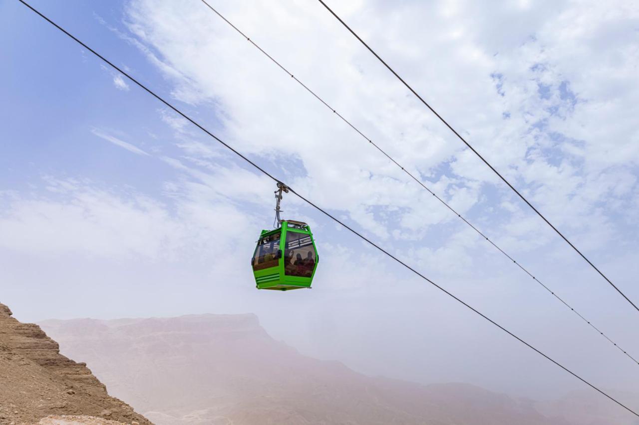 Tolip Resort El Galala Majestic Ain Sukhna Exterior photo The photo shows a green cable car suspended in the air, traveling along overhead cables. The backdrop features a hazy landscape, likely mountainous or elevated terrain, with a cloudy sky. The scene suggests a scenic transportation method, possibly us
