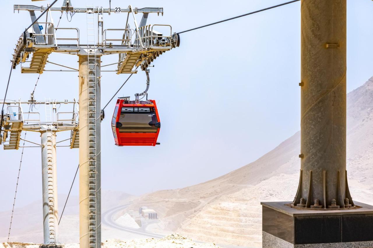 Tolip Resort El Galala Majestic Ain Sukhna Exterior photo The photo shows a cable car system with a single red gondola suspended mid-air. It appears to be part of a larger cable car infrastructure, with metal pylons supporting the cables above. The background features a hazy landscape, likely characterized 
