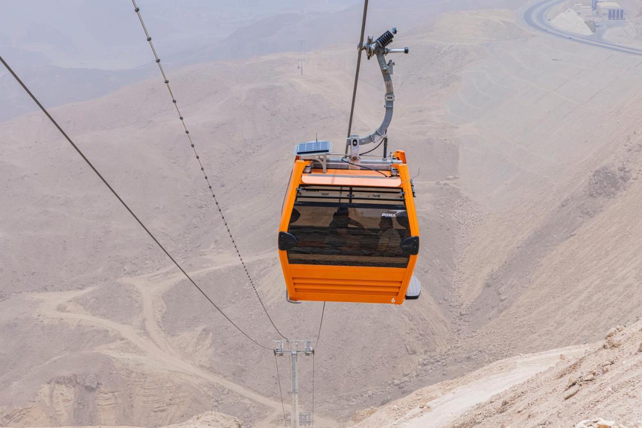 Tolip Resort El Galala Majestic Ain Sukhna Exterior photo The photo shows an orange cable car suspended in the air, traveling along a set of cables. It appears to be located in a mountainous or hilly area, with rugged terrain and dry, rocky landscapes visible below. The background features slopes that seem 