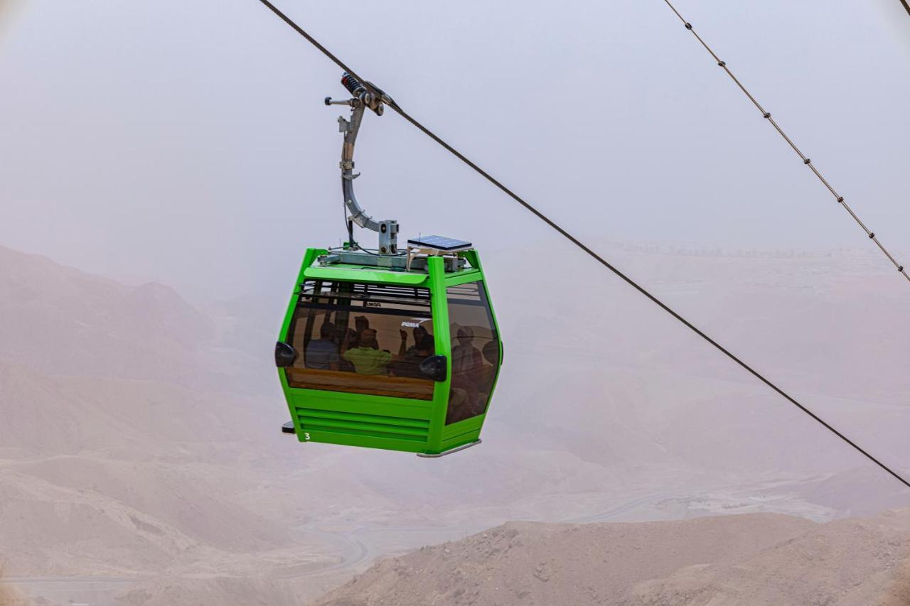 Tolip Resort El Galala Majestic Ain Sukhna Exterior photo The photo shows a green cable car suspended in the air, moving along a wire. The cable car appears to be traversing a mountainous landscape, which looks rocky and arid. The surrounding environment is somewhat foggy or hazy, suggesting limited visibil
