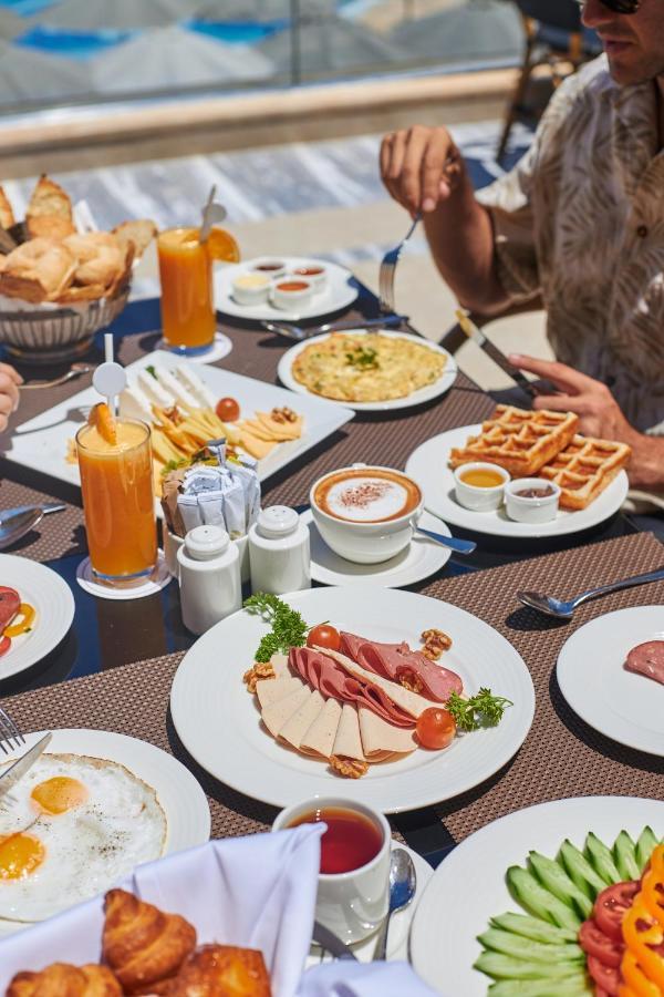 Tolip Resort El Galala Majestic Ain Sukhna Exterior photo The photo shows a breakfast spread laid out on a table. There are several plates with a variety of food items, including:

1. **Sliced Cold Cuts**: A plate featuring various cold meats, accompanied by garnishes like cherry tomatoes and lettuce.
2. **
