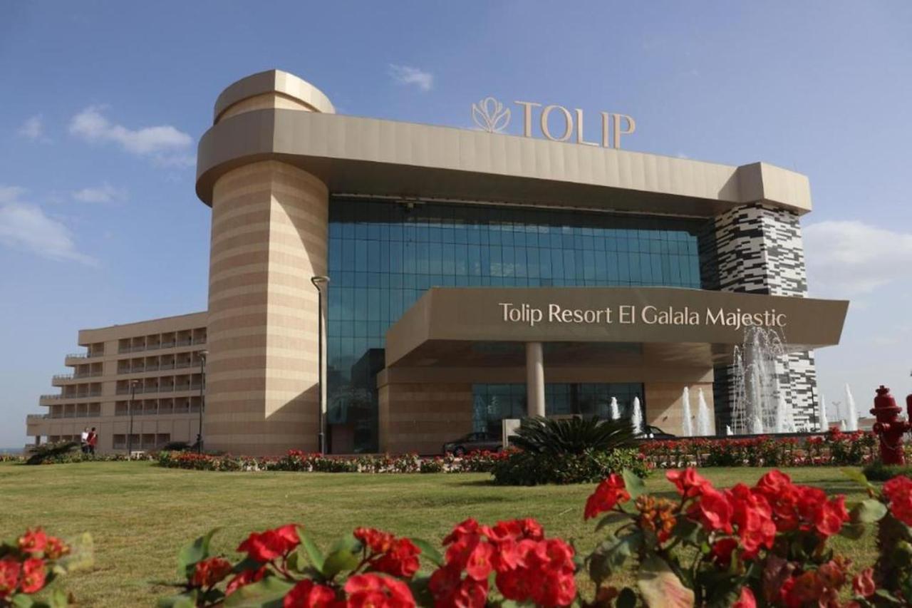Tolip Resort El Galala Majestic Ain Sukhna Exterior photo The photo shows a modern hotel building named "Tolip Resort El Galala Majestic." The structure features a distinctive architectural design with large glass windows and a prominent entrance. Surrounding the building are well-maintained lawns and vibra