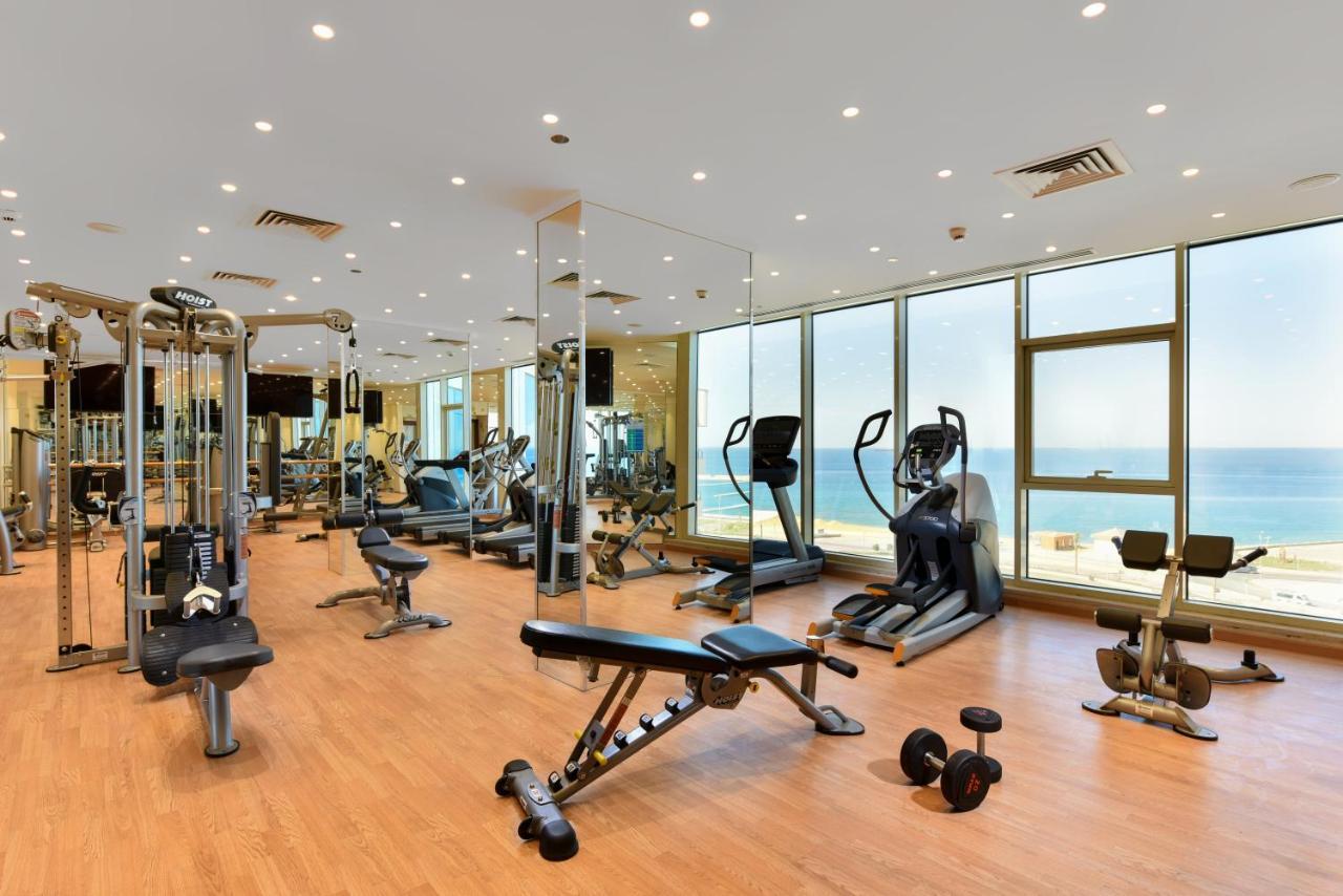 Tolip Resort El Galala Majestic Ain Sukhna Exterior photo The photo shows a modern gym interior with a variety of fitness equipment. There are cardio machines like treadmills and ellipticals, along with strength training equipment such as free weights and benches. The gym features large windows that offer a