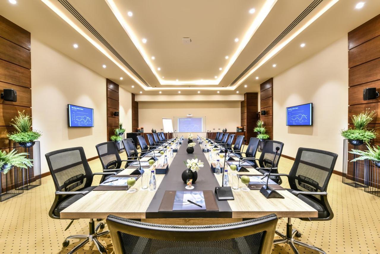 Tolip Resort El Galala Majestic Ain Sukhna Exterior photo The photo shows a modern conference room designed for meetings. It features a long rectangular table at the center, surrounded by ergonomic black chairs. The room is well-lit with ceiling lights and has a neutral color scheme. There are two large scr