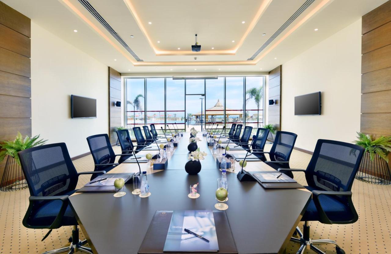 Tolip Resort El Galala Majestic Ain Sukhna Exterior photo The image shows a modern conference room with a large, dark rectangular table surrounded by ergonomic black chairs. The room features large windows that allow natural light to enter and provide a view of the outdoors, including some greenery. On the 