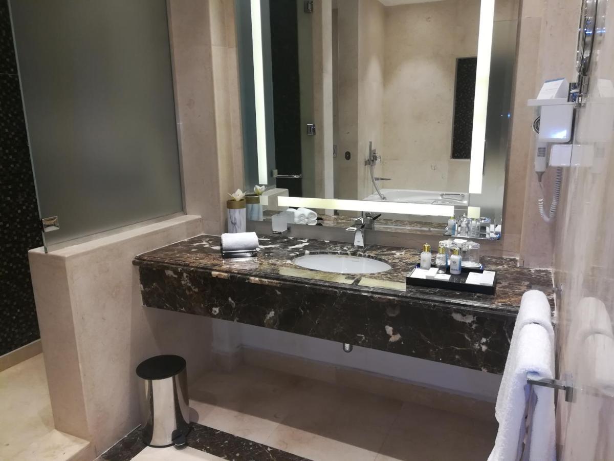 Tolip Resort El Galala Majestic Ain Sukhna Exterior photo The photo shows a modern bathroom with elegant design features. There is a large vanity made of dark marble with a sink and a set of toiletries neatly arranged on top. A mirror with built-in lighting is mounted above the sink. To the side, there is a