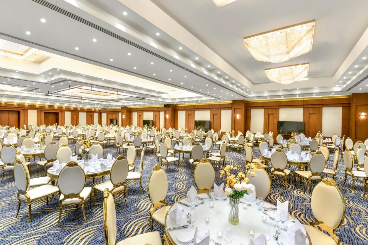 Tolip Resort El Galala Majestic Ain Sukhna Exterior photo The photo shows a spacious and elegantly decorated banquet hall. The room features numerous round dining tables, each set with white tablecloths and adorned with decorative centerpieces, likely flowers. The chairs surrounding the tables have a luxuri
